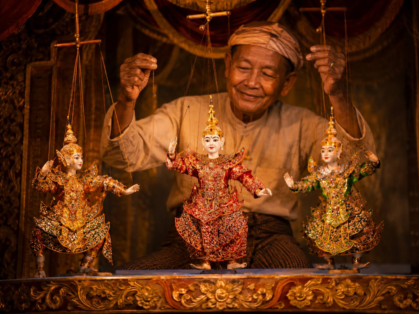 Artisan operating ornate traditional puppets on a carved stage.